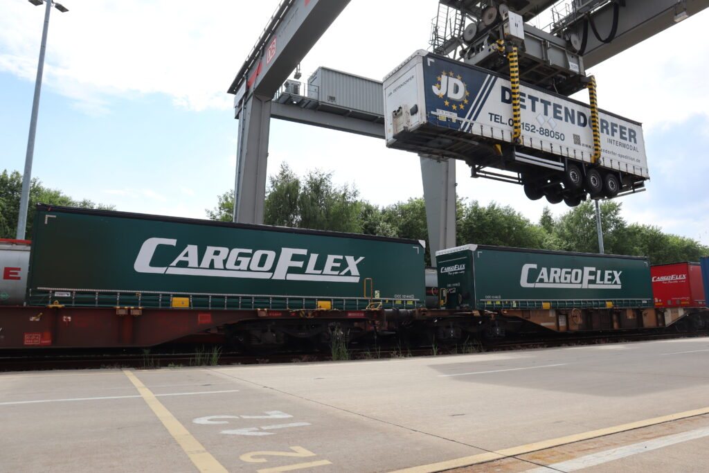 A gantry crane lifts a trailer onto a train, next to CargoFlex trailers already on their rail wagons